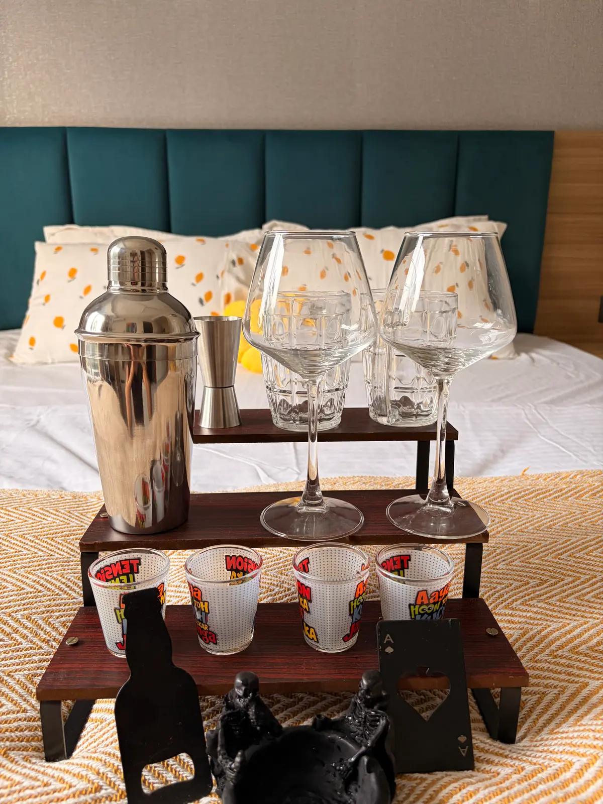 Cocktail shaker, glasses and shot glasses set out on the bed